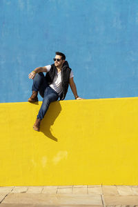 Bearded man in white t-shirt, jacket and jeans against blue background