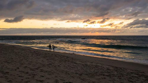 Silhouette person standing on beach against sky during sunset