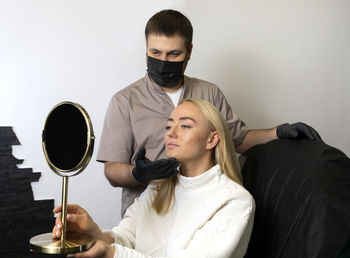 Portrait of young woman with headphones while sitting against wall