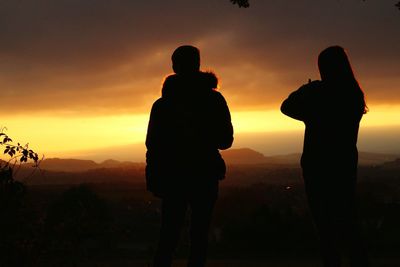 Silhouette couple standing on landscape against sky during sunset