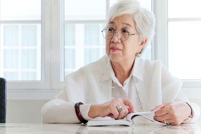 Senior woman with book sitting at home