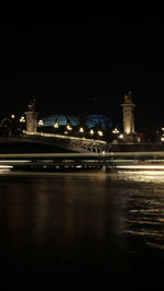 Illuminated city by river against sky at night