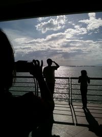 Silhouette people photographing sea against sky