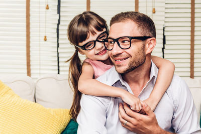 Daughter embracing father sitting on sofa at home