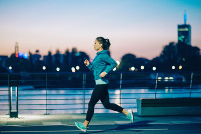 Young woman exercising on promenade by river against clear sky during sunset