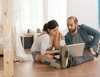 Young woman using phone while sitting on wooden floor