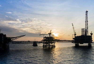 Cranes at commercial dock against sky during sunset