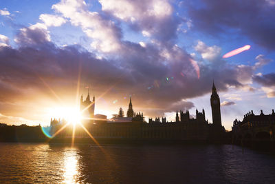 Silhouette big ben and houses of parliament by thames river against cloudy sky