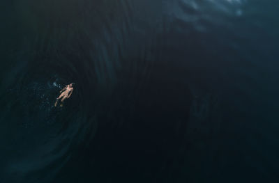 A naked young girl swims in the dark sea. aerial view. in harmony with nature