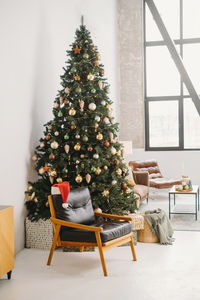 Cozy armchair near christmas tree in sunny room . santa's hat in the morning. nobody christmas tree