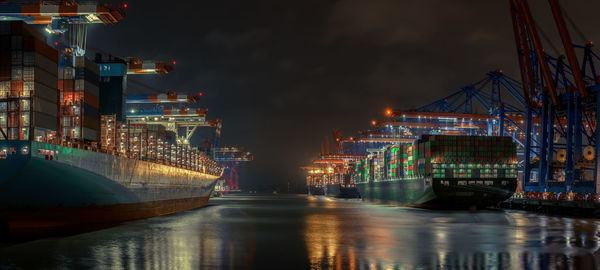 Illuminated city by river against sky at night