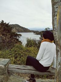 Rear view of woman sitting on shore against sky
