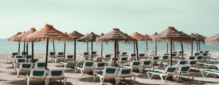 Lounge chairs and parasols on beach against sky