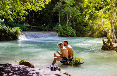 Men sitting at shore against trees