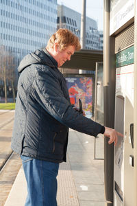 Side view of man standing on mobile phone in city