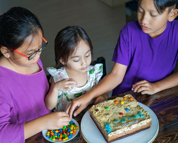 High angle view of cute siblings sitting by cake at home