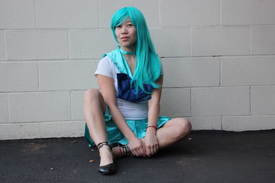 Portrait of woman with blue hair sitting on road against wall