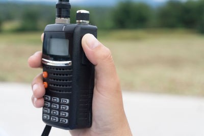 Close-up of hand holding walkie-talkie against sky