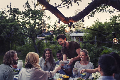 Happy man serving water to friend during dinner party at yard