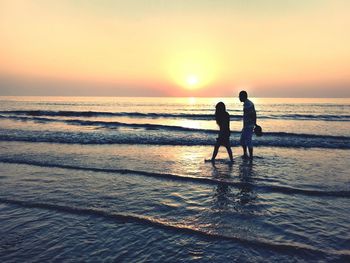 Silhouette men on beach against sky during sunset