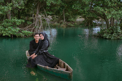 Portrait of a young man sitting on lake against trees