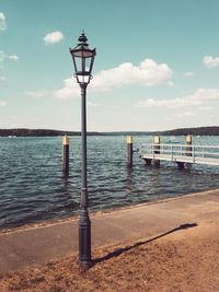 Street light on wooden post by sea against sky