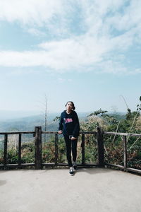 Full length portrait of woman standing on railing against sea