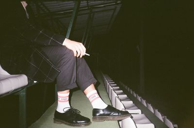 Low section of man smoking cigarette while sitting on chair at stadium