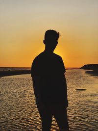 Man standing by sea against sky during sunset