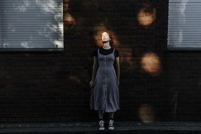 Teenage girl with eyes closed standing against brick wall