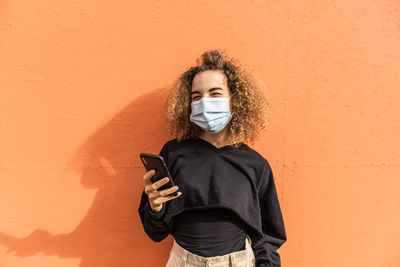 Portrait of man holding smart phone while standing against wall