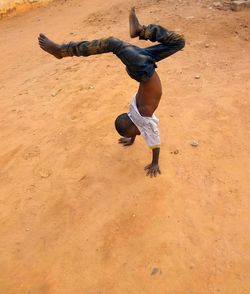 Rear view of boy with arms raised on sand