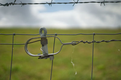 Close-up of barbed wire fence on field against sky