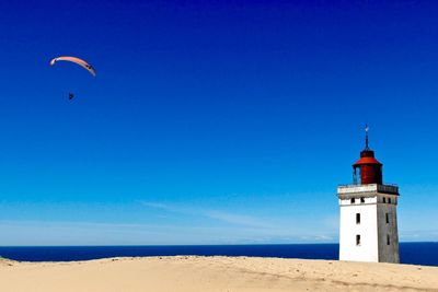 Low angle view of lighthouse on beach against clear blue sky