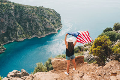 Woman standing on rock and waving  us flag. traveler standing on mountain. 4 july independence day