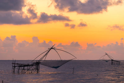 Fishing equipment on sea against sky during sunset