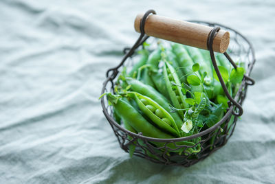 Basket with young fresh juicy pods of green peas on a green textile background. 