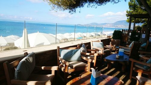 Empty chairs and tables at restaurant by sea against sky