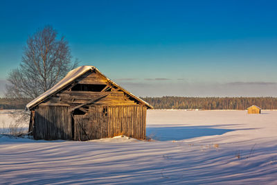 House on snow covered field against blue sky