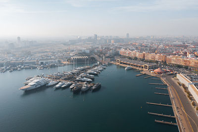 Aerial scenic view of modern city near serene harbor with moored boats in industrial port of valencia