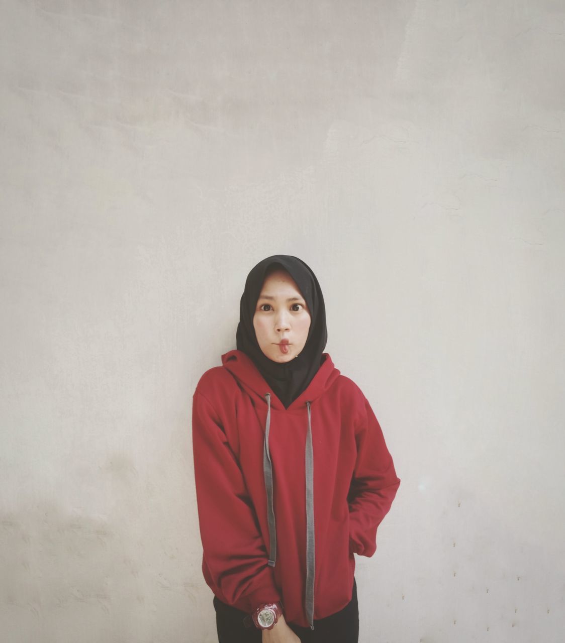 one person, front view, looking at camera, standing, real people, young adult, young women, portrait, wall - building feature, clothing, lifestyles, leisure activity, casual clothing, red, waist up, three quarter length, indoors, beautiful woman, hood - clothing, contemplation