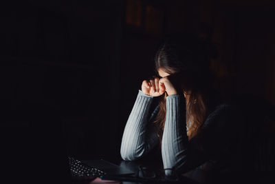 Side view of young woman looking away against black background