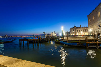 River by illuminated city against blue sky at night