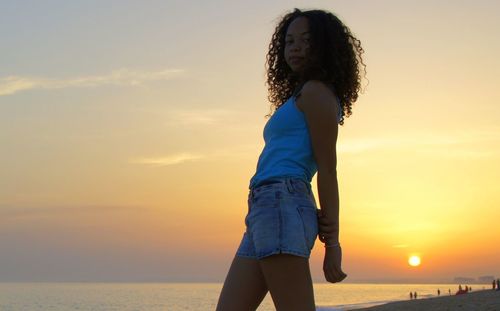 Woman standing at beach against sky during sunset