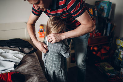 Midsection of father with son standing on bed at home