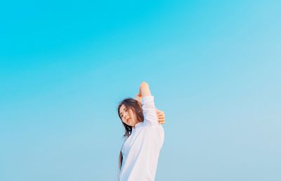 Low angle view of woman standing against clear blue sky