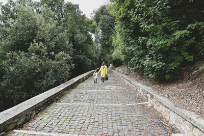 Full length of mother with daughter walking on footpath amidst trees