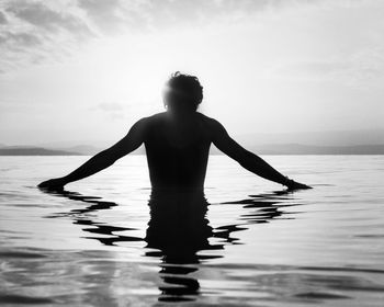 Rear view of shirtless man in sea against sky