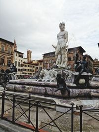 Statue by buildings against sky