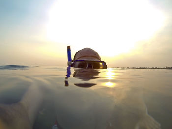 Close-up of person swimming in sea against sunset sky